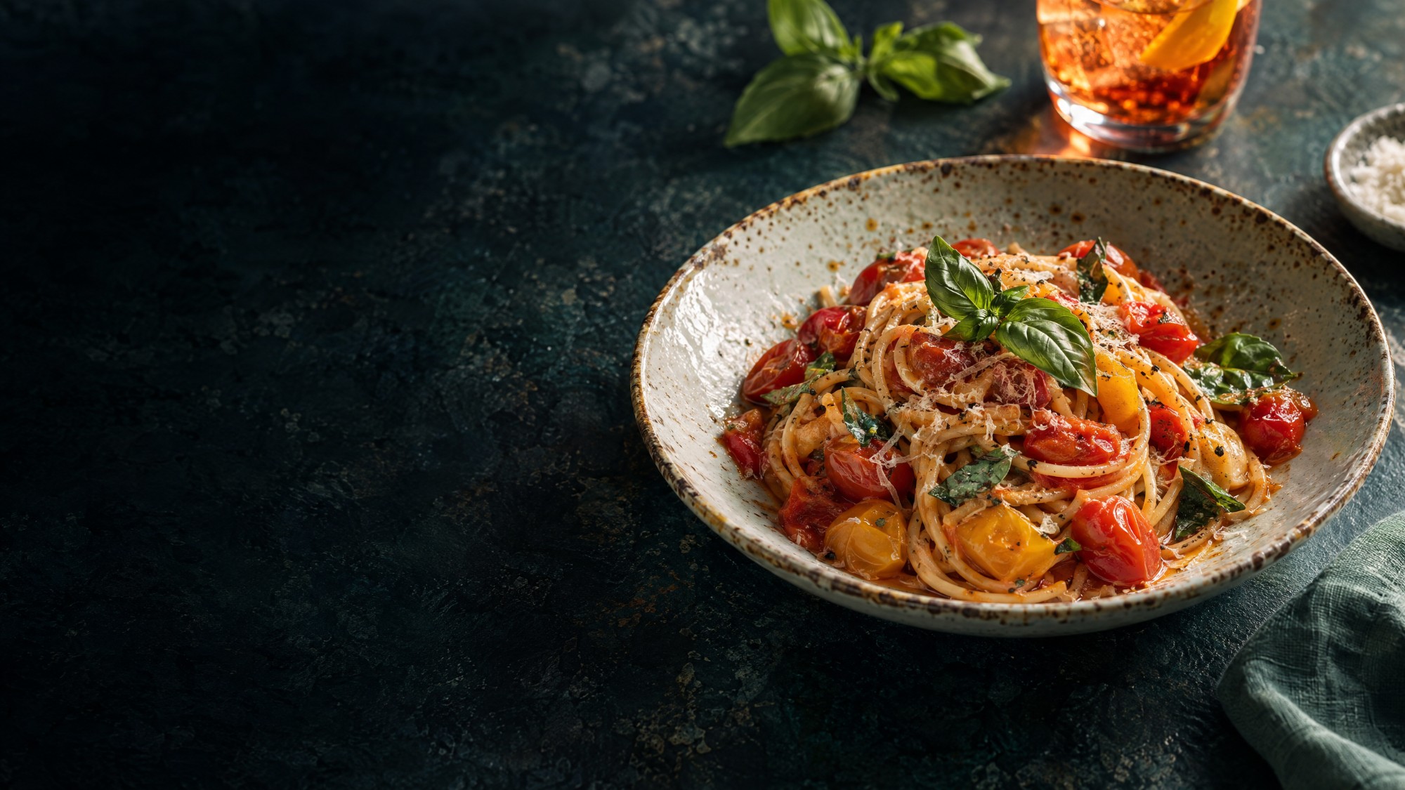 Spaghetti with red and yellow cherry tomatoes and basil in a ceramic bowl.